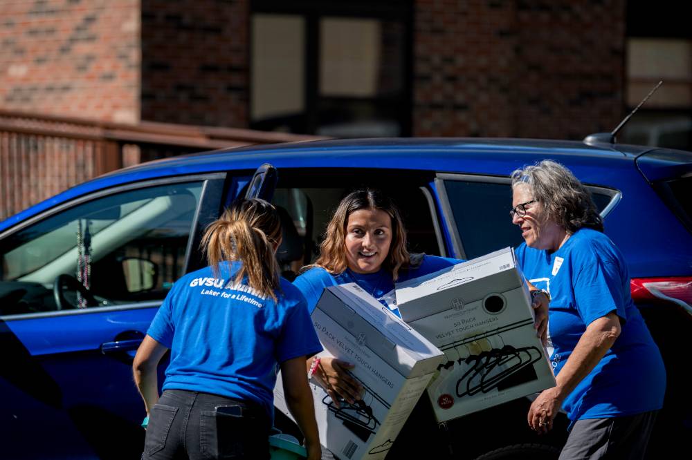 Three alumni carrying boxes out of car